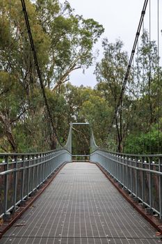 A large steel suspension foot bridge over a river nestled in the Australian bush.