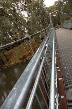 A large steel suspension foot bridge over a river nestled in the Australian bush.