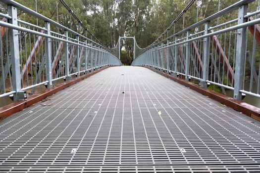 A large steel suspension foot bridge over a river nestled in the Australian bush.