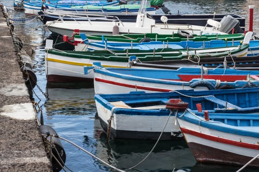 Several small colorful boats are anchored in the harbor of Catania, SIcily-Italy on the coast of the Mediterranean Sea.