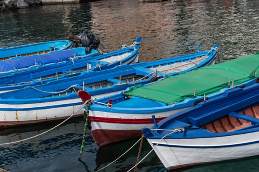 Several small colorful boats are anchored in the harbor of Catania, SIcily-Italy on the coast of the Mediterranean Sea.