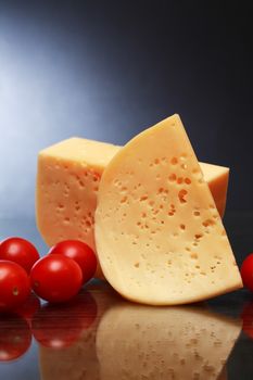 Piece of cheese and tomatoes on nice dark background with reverberation