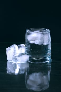 Glass of water with ice cubes on nice dark background