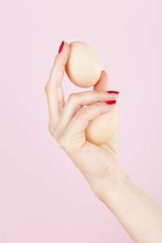 Erectile dysfunction, impotence. Female hand with red fingernails holding two eggs isolated on pink background.