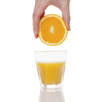 Freshly squeezed orange juice. Female hand squeezing orange into a glass isolated on white background. Healthy juice drink.  