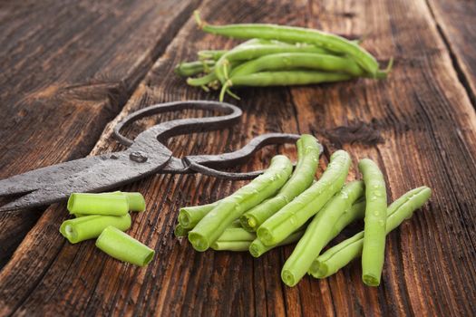 Raw fresh green beans with water drops on brown wooden textured table. Fresh vegetable eating. 