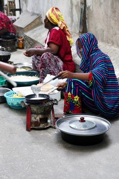 Stone Town, Zanzibar, Tanzania - January 1, 2016:  Street in Stone Town Seated Woman with show cooking