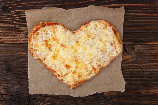 Delicious pizza in heart shape on wooden table, top view. Culinary pizza eating.
