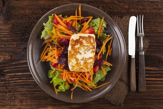 Colorful fresh salad with grilled halloumi cheese with on plate on wooden table, top view. Culinary delicious vegetarian eating, mediterranean style.