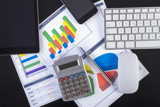 Modern workplace with digital tablet, pen, keyboard, mouse, smartphone and paper showing charts and diagram numbers on table.