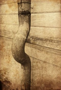 Textured rusty rain pipe against wooden facade pointing left.