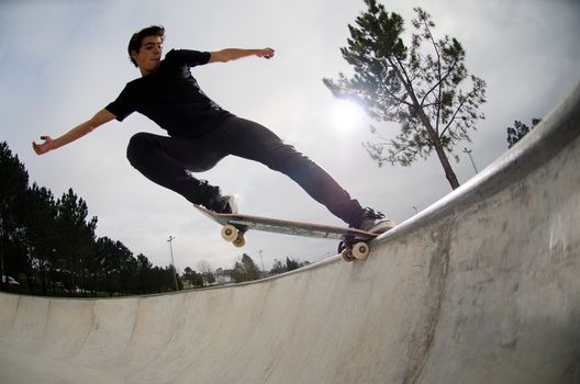 Skateboarder doing a tail slide on a croncrete pool at the skate park.