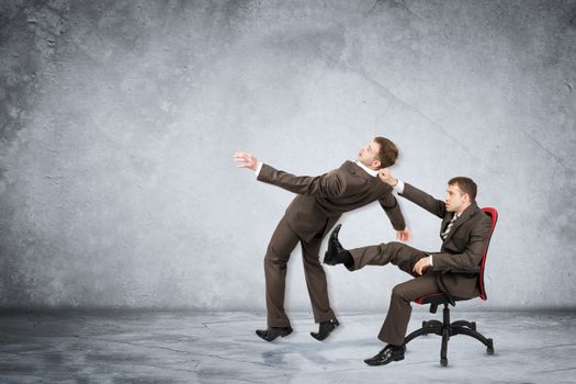 Businessman sitting on chair and kicking man on grey wall background