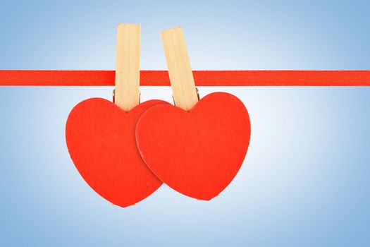 Valentine day template, two red wooden hearts with clothes pins on textile ribbon over sky blue grain noise gradient