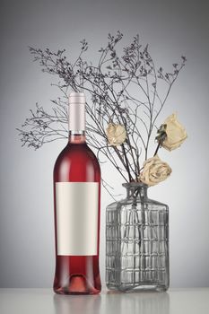 Rose wine bottle with label mockup to withered white roses in a vase.
