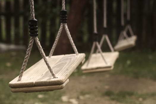 Horizontal perspective view of three wooden child swings in the park with shallow depth of field