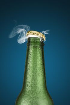 Green cold beer bottle with water drops and golden cap open on blue background