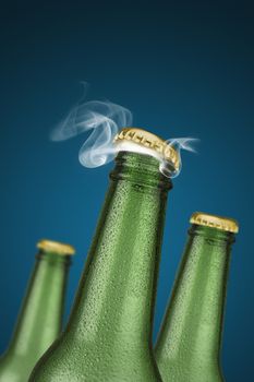 Green cold beer bottles with water drops and golden cap open on blue background