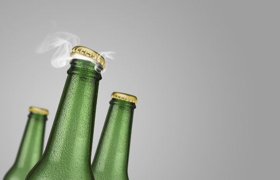 Horizontal photo of three green cold beer bottles with water drops and golden cap open on grey background