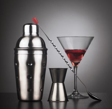 Cocktail tools with shaker, spoon and a glass filled with red liquid,  square composition