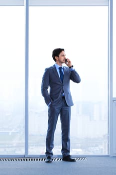 Businessman standing near window, looking at city and talking by phone