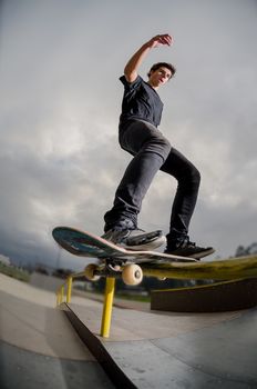 Skateboarder doing a board slide over the rail at the skate park.