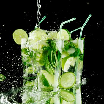 Pouring fresh mojito cocktail in glasses isolated on black background