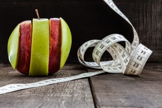 The image shows apple surrounded by a measuring tape referring to diet and health concept on wooden background