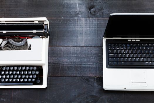 The image represents a retro typewriter and a laptop on a dark wood background conceptualizing that the time of technology is getting older the picture is taken from a top view