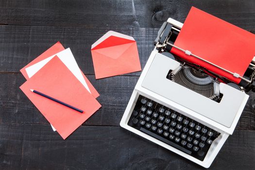 The image represents a retro typewriter , a vintage red telephone and some coloured paper on a dark wood background with a rede paper conceptualizing this colour like danger, love or something different