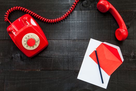 The image represents a retro typewriter , a vintage red telephone and some coloured paper on a dark wood background with a rede paper conceptualizing this colour like danger, love or something different