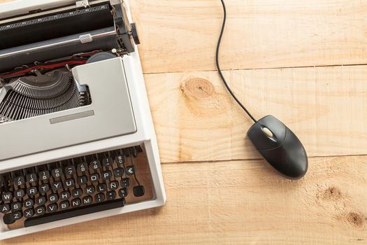 The image shows an antique typewriter connected to a computer mouse imitating a laptop and conceptualizing the obsolescence of technology