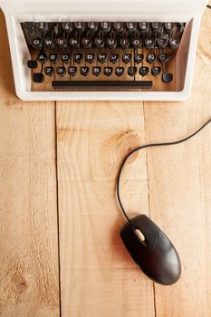 The image shows an antique typewriter connected to a computer mouse imitating a laptop and conceptualizing the obsolescence of technology