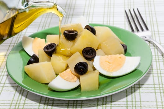 Dish of potato salad, egg and black olives with olive oil