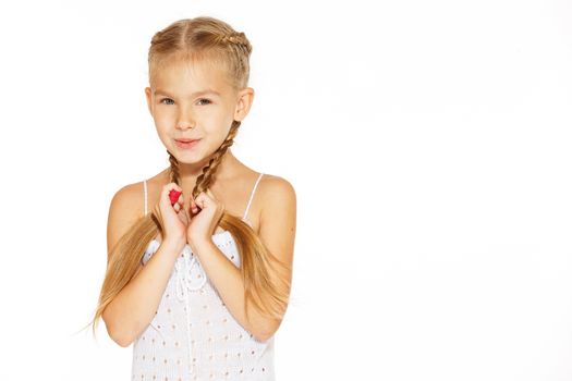 Funny little girl with a charming smile in a white dress holding a pigtails