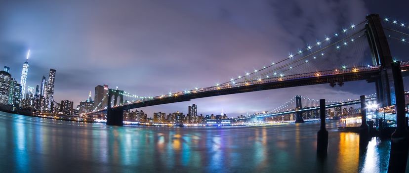 Manhattan bridge and New York City downtown skyline at dusk with skyscrapers illuminated over East River panorama. 