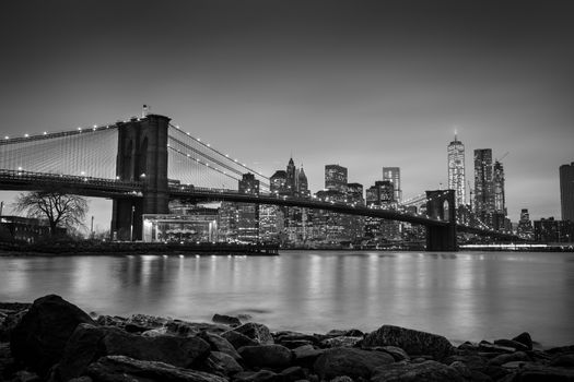 Brooklyn bridge and New York City Manhattan downtown skyline at dusk with skyscrapers illuminated over East River panorama. Copy space. Black and white image.