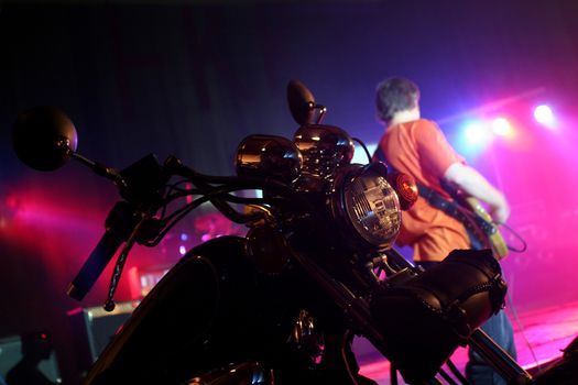 Chopper motocycle on stage witha guitarist on the background