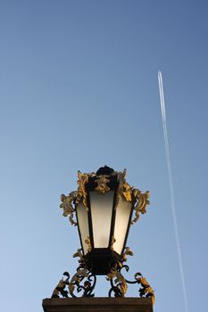 Old beautiful baroque street (in Warsaw) lamp with airline trail in the back