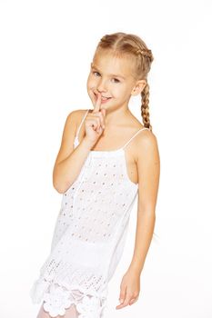 Funny little girl with a charming smile in a white dress showing silence sign