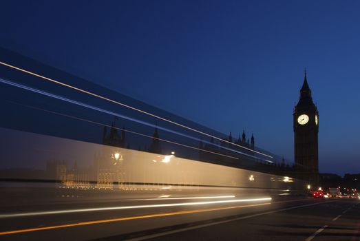 Night silhouette of Big Ben and light trail of a bus in front.