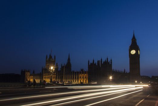 Night silhouette of Big Ben and light trail of a bus in front.