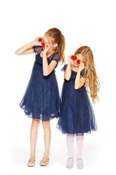 Little cute girls holding two red flowers near their eyes