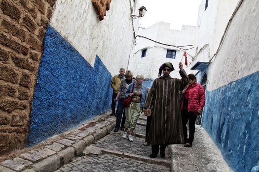 Rabat, Morocco - March 10, 2011: Local guide and a group of tourist wandering on the blue streets of old medina in Rabat.