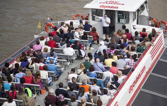 Tourists with boat on Thames River listening to their guide.