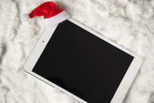 Digital tablet with santa hat surrounded by white cotton