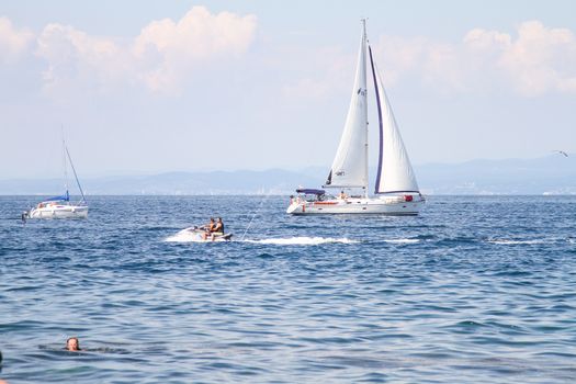 Yacht and people on water scuter by the coast.