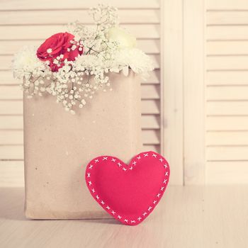 Flowers in paper bag with red ribbon on wooden background