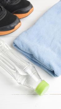 fitness equipment:blue towel,drinking water and running shoes on white wood table