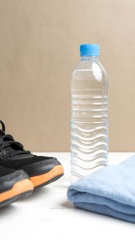 fitness equipment:blue towel,drinking water and running shoes on white wood table